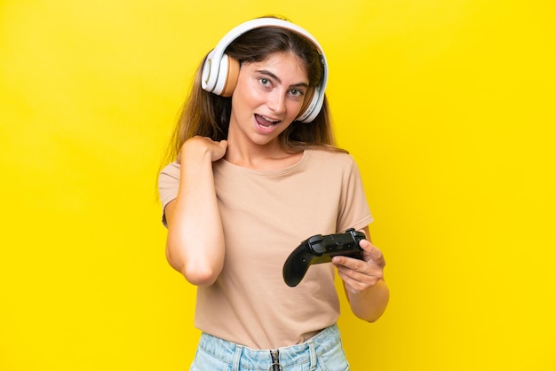 Young caucasian woman playing with a video game controller isolated on yellow background laughing