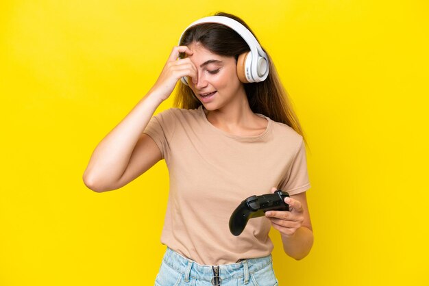 Young caucasian woman playing with a video game controller isolated on yellow background laughing