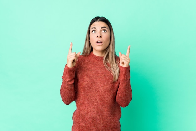 Young caucasian woman pointing upside with opened mouth.