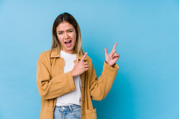 Young caucasian woman pointing with forefingers to a copy space, expressing excitement and desire.