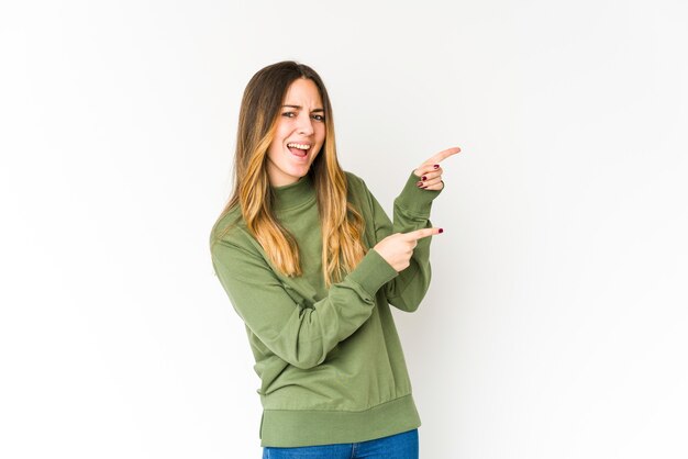 Young caucasian woman pointing with forefingers to a copy space, expressing excitement and desire.