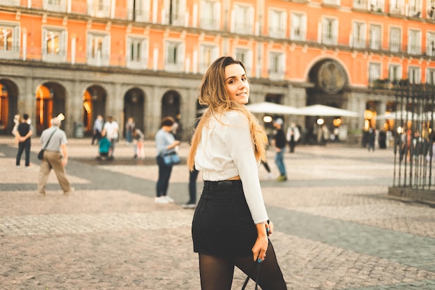 Young caucasian woman portrait with a white blouse and a black skirt at Madrid's Plaza Mayor, Spain.