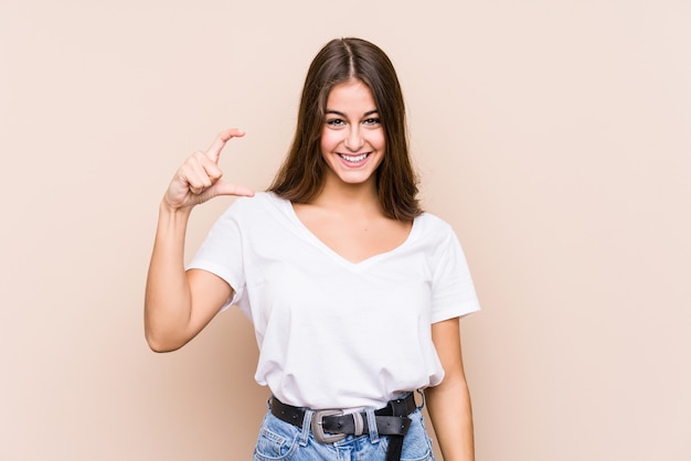 Young caucasian woman posing isolated holding something little with forefingers, smiling and confident.