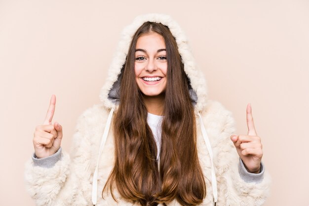 Young caucasian woman posing isolated indicates with both fore fingers up showing a blank space.