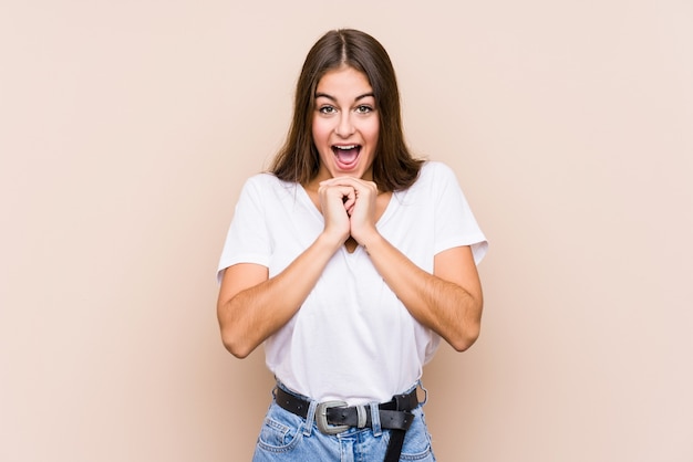 Young caucasian woman posing isolated praying for luck, amazed and opening mouth looking to front.