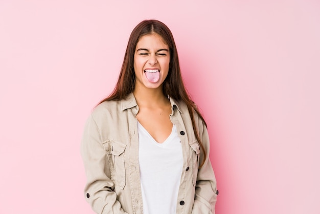 Young caucasian woman posing in a pink wall funny and friendly sticking out tongue.