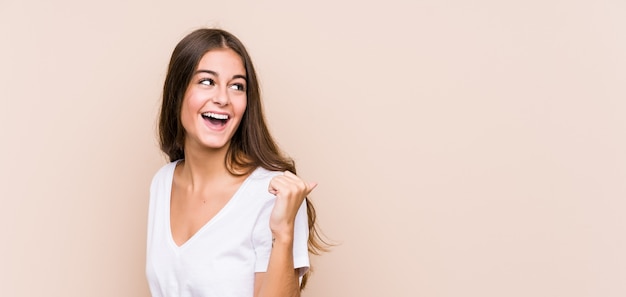 Young caucasian woman posing points with thumb finger away, laughing and carefree.