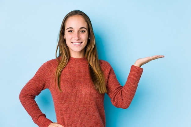 Foto giovane donna caucasica che propone mostrando uno spazio in bianco su una palma e che tiene un'altra mano sulla vita.