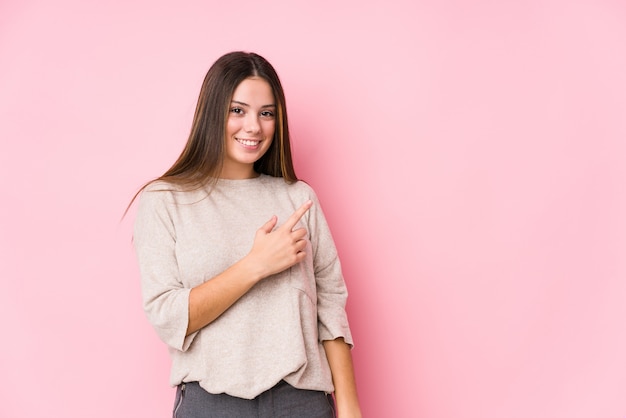 Young caucasian woman posing smiling and pointing aside, showing something at blank space.