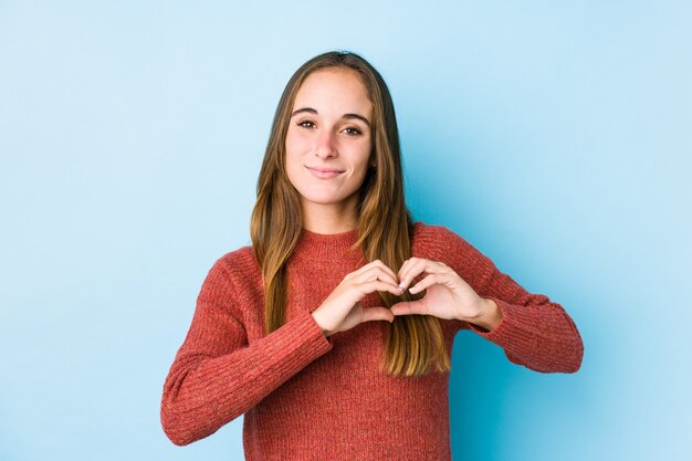 Young caucasian woman posing   smiling and showing a heart shape with hands.