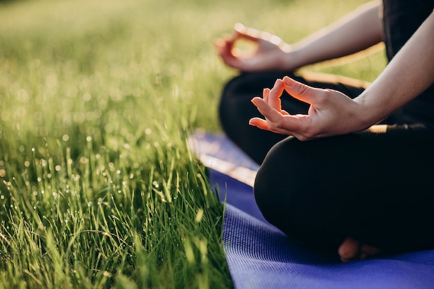 Young caucasian woman practices yoga in lotus position on an early sunny morning in a forest with grass and dew Soft selective focus.