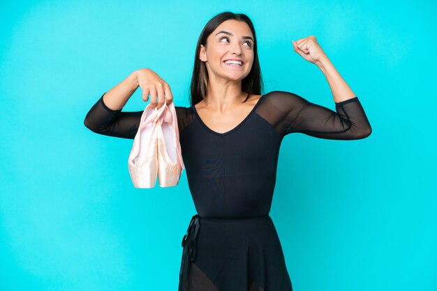 Young caucasian woman practicing ballet isolated on blue background doing strong gesture