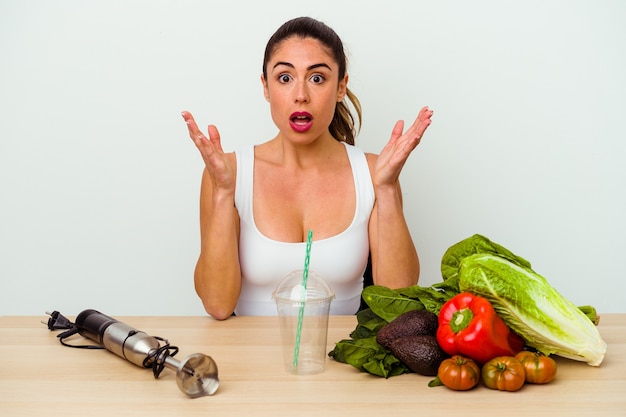 Young caucasian woman preparing a healthy smoothie with vegetables surprised and shocked.