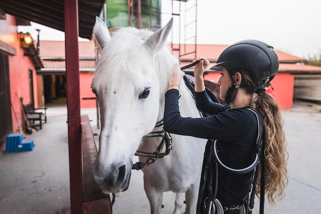 Young caucasian woman preparing a white horse for a ride