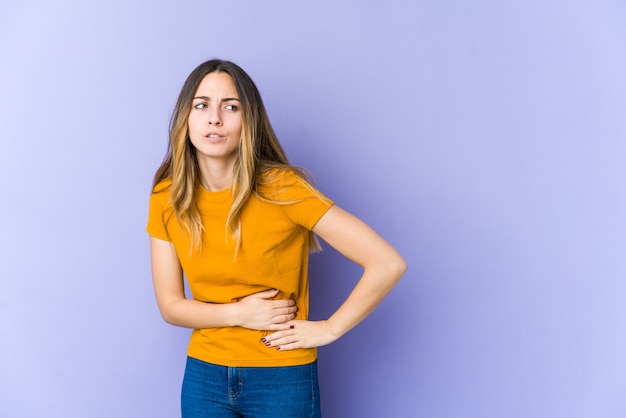 Young caucasian woman on purple having a liver pain, stomach ache.