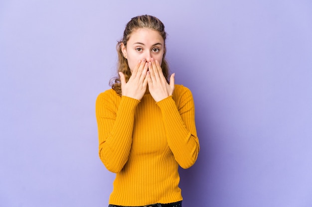 Young caucasian woman on purple shocked, covering mouth with hands, anxious to discover something new.