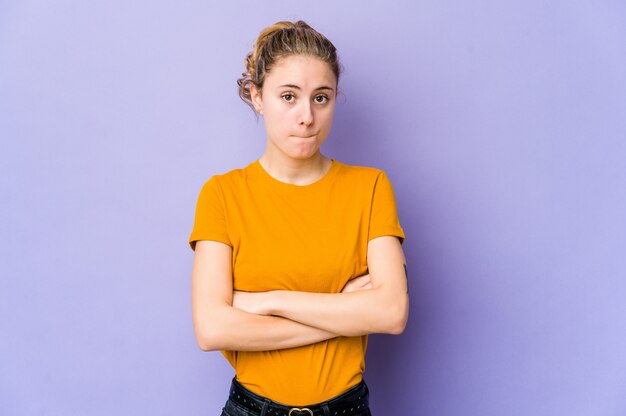 Young caucasian woman on purple shrugs shoulders and opon eyes confused.