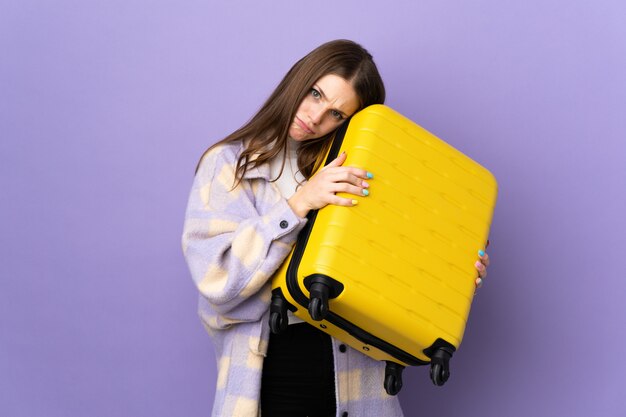 Молодая кавказская женщина на пурпуре в каникулах с чемоданом перемещения и несчастная