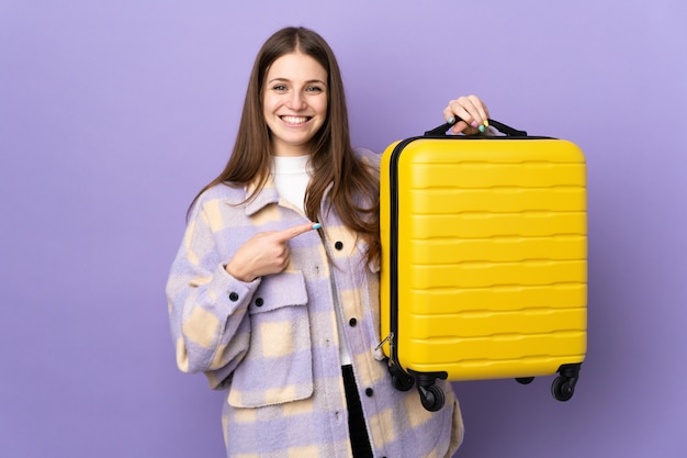 Young caucasian woman on purple in vacation with travel suitcase