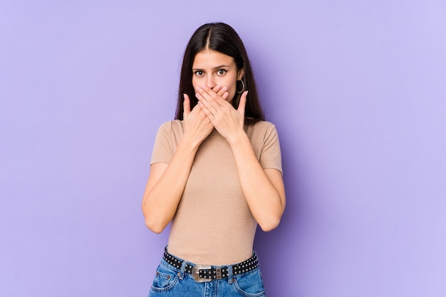 Young caucasian woman on purple wall covering mouth with hands looking worried.