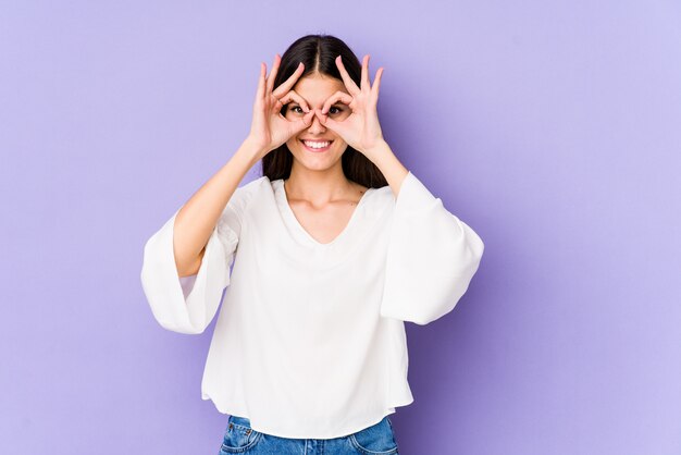 Young caucasian woman on purple wall excited keeping ok gesture on eye.