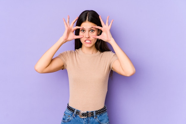 Young caucasian woman on purple wall keeping eyes opened to find a success opportunity.