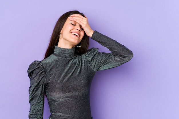 Young caucasian woman on purple wall laughs joyfully keeping hands on head