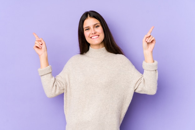 Young caucasian woman on purple wall pointing to different blank spaces, choosing one of them, showing with finger.