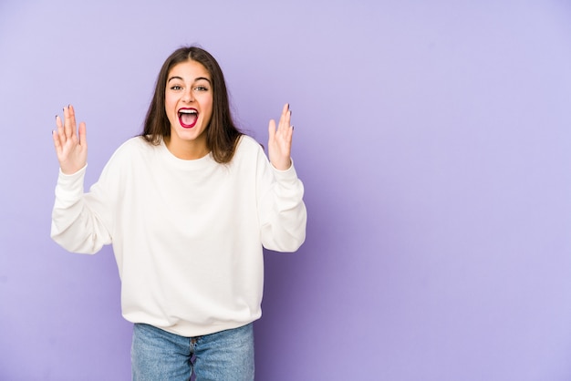 Young caucasian woman on purple wall receiving a pleasant surprise, excited and raising hands.