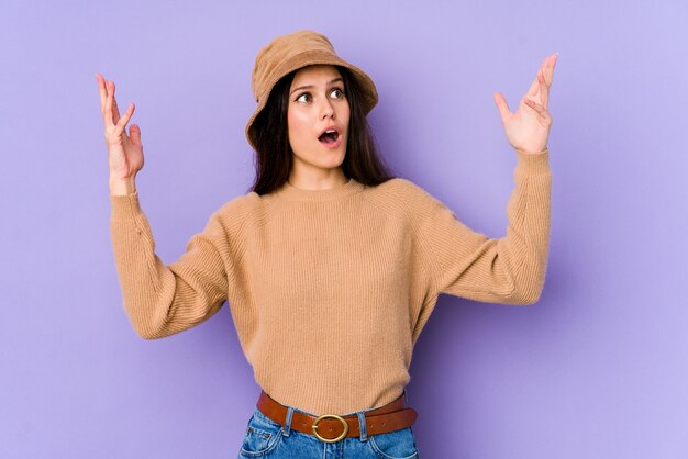 Young caucasian woman on purple wall screaming to the sky, looking up, frustrated.