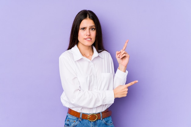 Young caucasian woman on purple wall shocked pointing with index fingers to a blank space