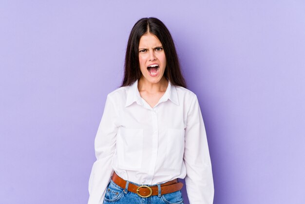 Young caucasian woman on purple wall shouting very angry