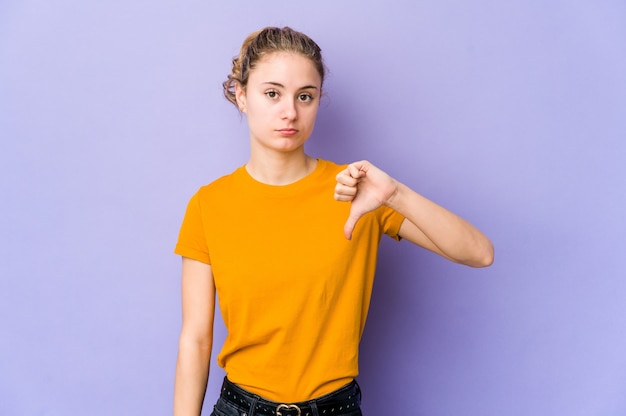 Young caucasian woman on purple wall showing a dislike gesture, thumbs down. Disagreement concept.