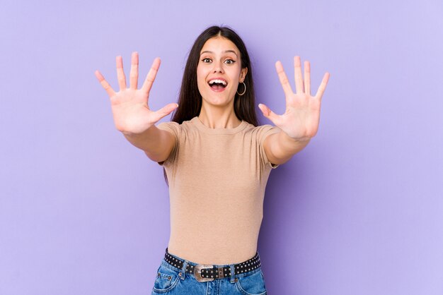 Young caucasian woman on purple wall showing number ten with hands.