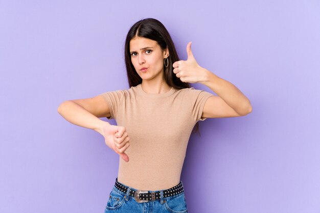 Young caucasian woman on purple wall showing thumbs up and thumbs down