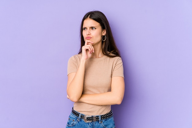 Young caucasian woman on purple wall thinking and looking up, being reflective, contemplating, having a fantasy.