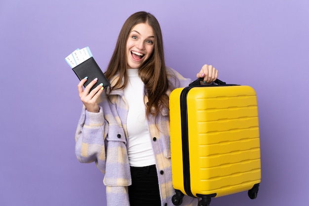 Young caucasian woman on purple wall in vacation with suitcase and passport