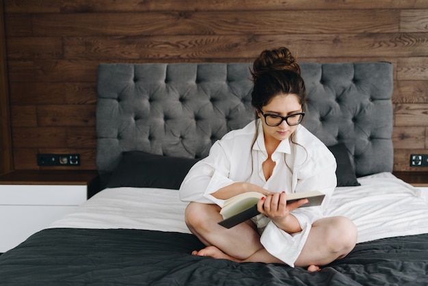 Young caucasian woman reading a book on her bed in her bedroom in the morning staying at home