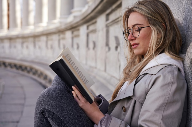 Молодая кавказская женщина читает книгу в парке со старинным зданием