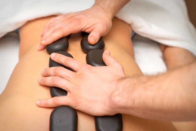 Young caucasian woman receiving back massage with black stones by masseur in spa salon. A woman getting a spa treatment.