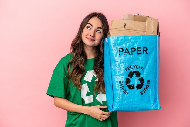 Young caucasian woman recycled paper isolated on pink background dreaming of achieving goals and purposes