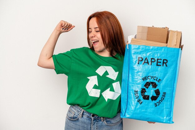 Young caucasian woman recycled paper isolated on white background raising fist after a victory, winner concept.