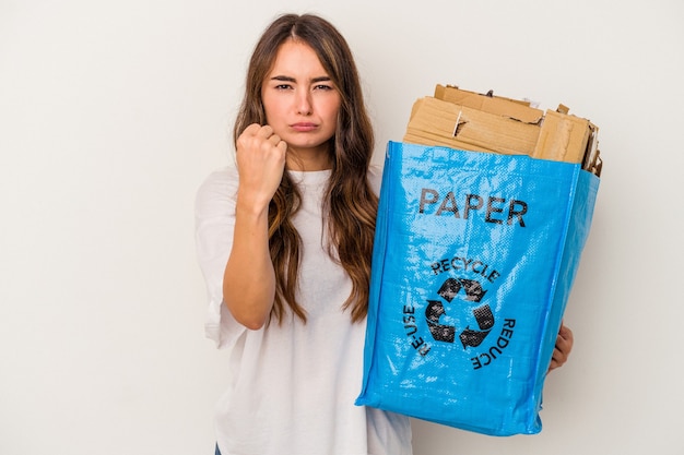 Young caucasian woman recycling paper isolated on white background showing fist to camera, aggressive facial expression.