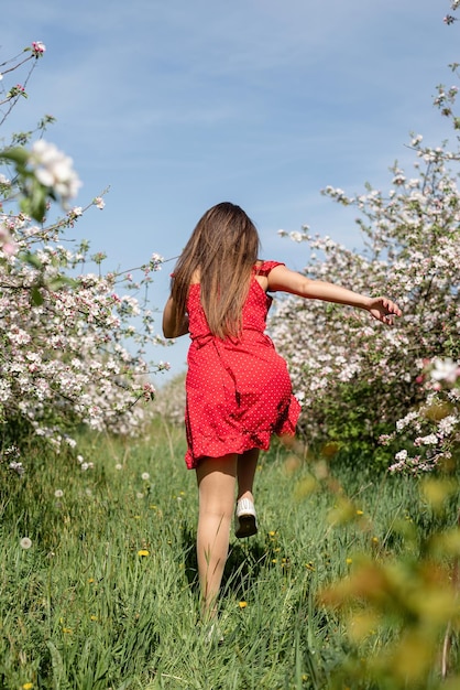 リンゴの木の開花を楽しんでいる赤いドレスを着た若い白人女性