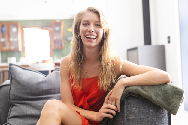 Photo young caucasian woman in a red dress smiles while seated on a couch