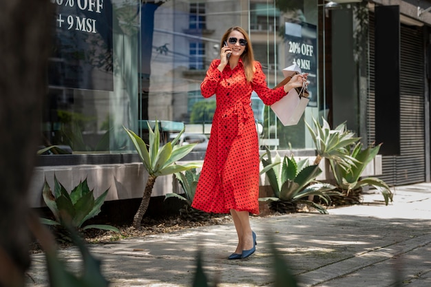 Молодая кавказская женщина в красном платье гуляет и делает покупки в городе