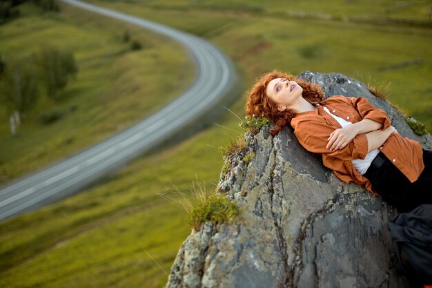 Photo young caucasian woman relax on rocky cliff and enjoying nature view travel and resting alone having ...