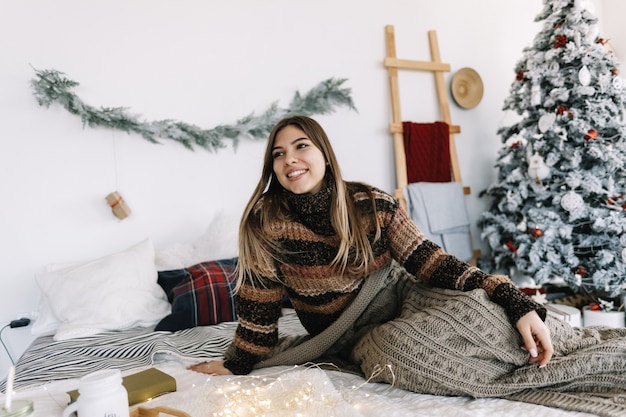 Young caucasian woman relaxing on a bed at home in Christmas holidays.