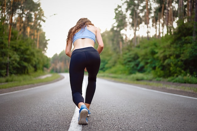 Young caucasian woman running asphalt road Sunny summer morning Rear view