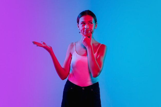 Young caucasian woman's portrait on gradient blue-purple studio background in neon light